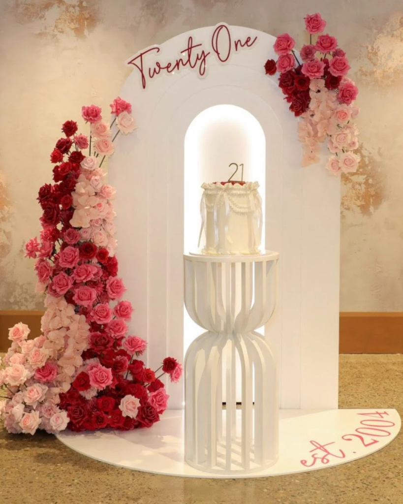 pink and berry coloured flower arrangement with white arch backdrop for 21st birthday